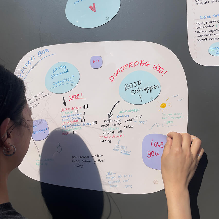 Vrouw plakt sticky note op organische Sticky blanco board extra groot Whiteboard van Greenstory geplakt op een kastdeur