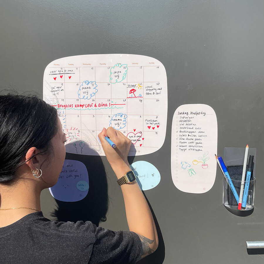 een dame schrijft op een organisch design sticky maandplanner, naast de maandplanner plakt er een to do lijst en een sticky bakje met pennen