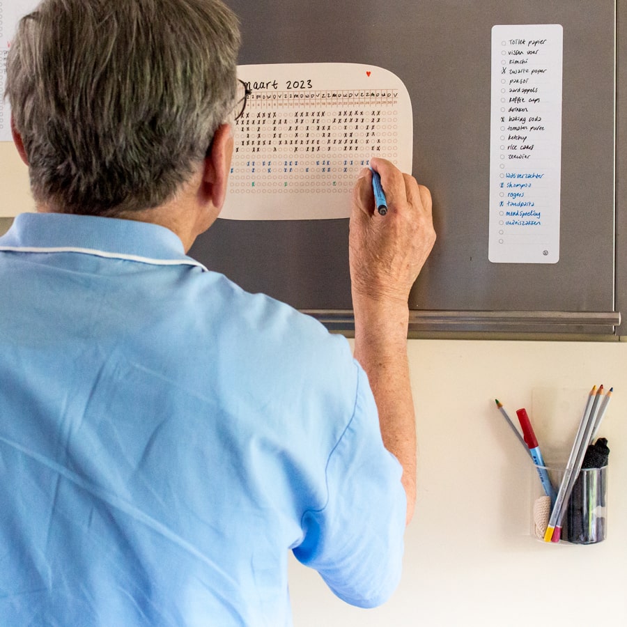 Man kijkt op de ingevulde Sticky Whiteboard habit tracker, ernaast een sticky boodschappenplanner.
